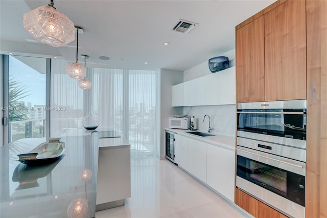 kitchen with decorative light fixtures, sink, white cabinets, beverage cooler, and stainless steel double oven