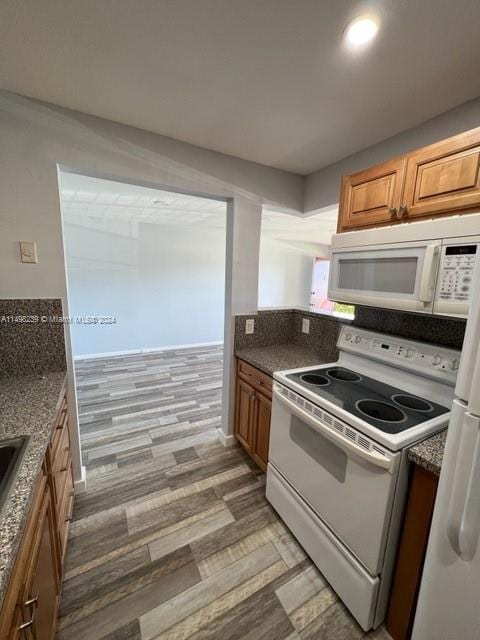 kitchen with dark stone counters, light hardwood / wood-style flooring, tasteful backsplash, and white appliances