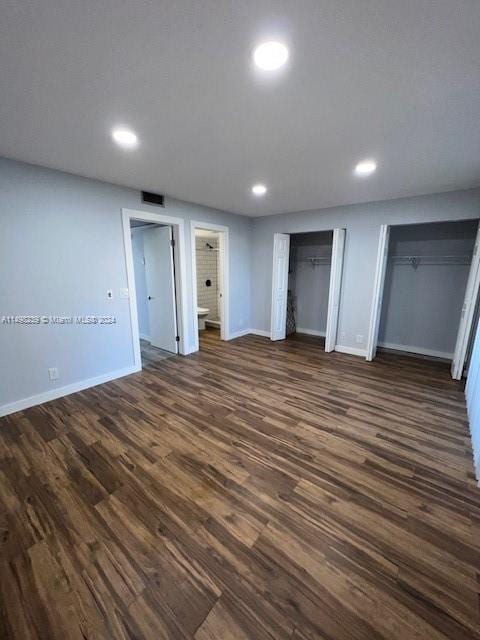 unfurnished bedroom featuring connected bathroom, two closets, and dark hardwood / wood-style flooring