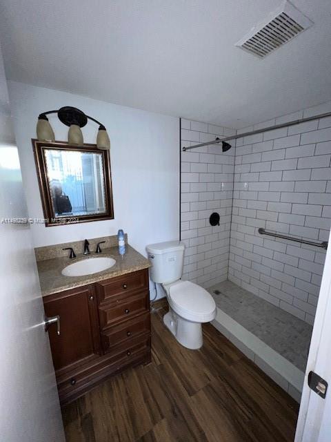 bathroom with toilet, vanity, tiled shower, and hardwood / wood-style flooring