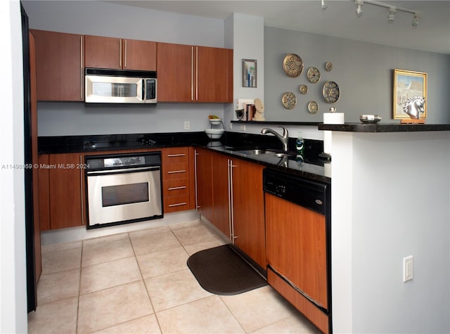 kitchen featuring a sink, light tile patterned flooring, a peninsula, appliances with stainless steel finishes, and brown cabinetry