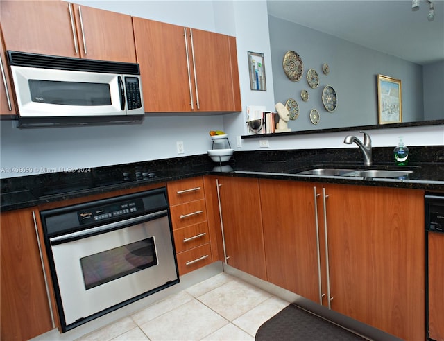 kitchen with appliances with stainless steel finishes, sink, kitchen peninsula, light tile patterned floors, and dark stone countertops