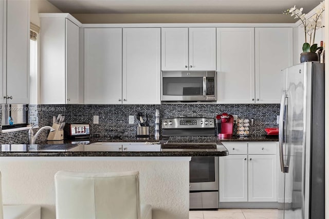 kitchen featuring white cabinets, a breakfast bar, backsplash, and appliances with stainless steel finishes