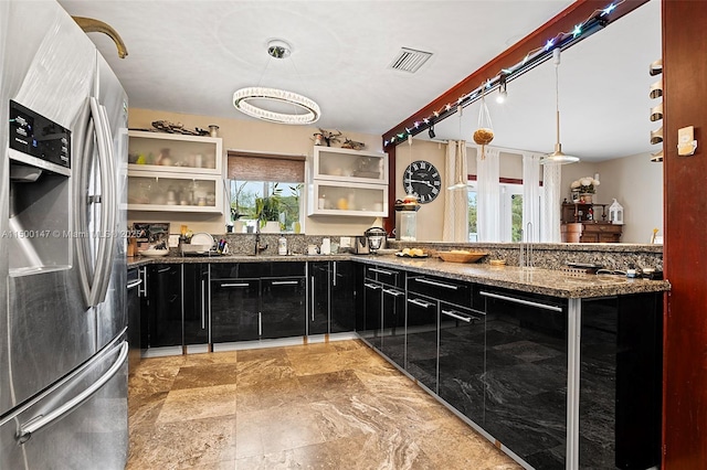 kitchen with decorative light fixtures, a healthy amount of sunlight, stainless steel fridge, and dark stone countertops