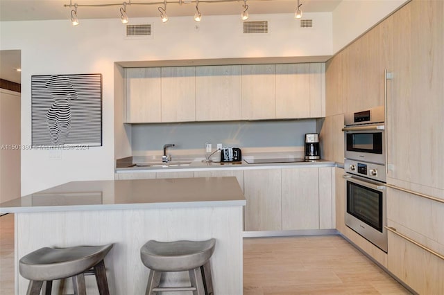 kitchen with rail lighting, stainless steel double oven, light hardwood / wood-style floors, and light brown cabinets