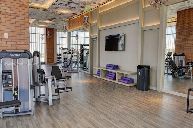 workout area featuring brick wall, expansive windows, wood-type flooring, and plenty of natural light