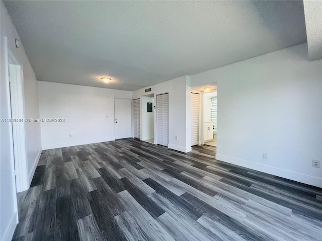 unfurnished bedroom featuring two closets, dark hardwood / wood-style floors, and a textured ceiling