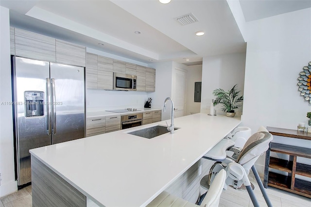 kitchen with kitchen peninsula, sink, light tile floors, stainless steel appliances, and a kitchen bar