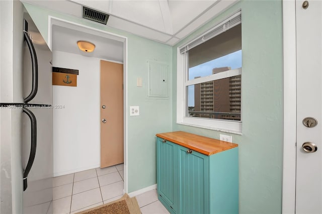 kitchen featuring wood counters, stainless steel fridge, light tile patterned flooring, and electric panel