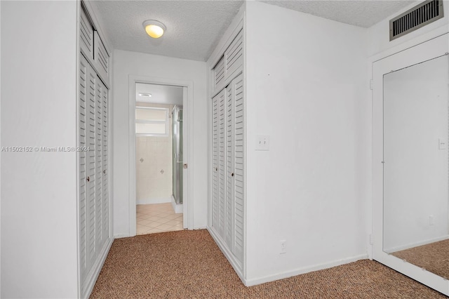 corridor with a textured ceiling and light carpet