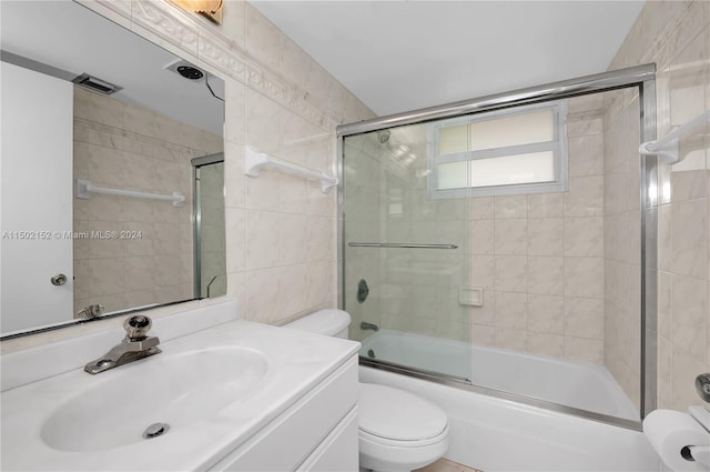 full bathroom featuring toilet, combined bath / shower with glass door, and vanity