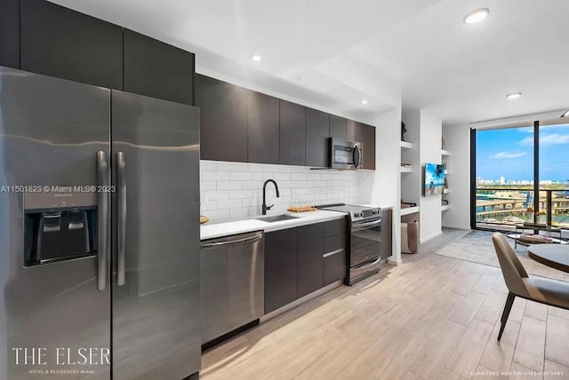 kitchen featuring expansive windows, appliances with stainless steel finishes, light hardwood / wood-style floors, sink, and tasteful backsplash