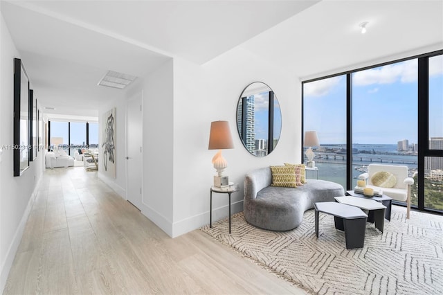 sitting room featuring floor to ceiling windows, light wood-type flooring, and a water view