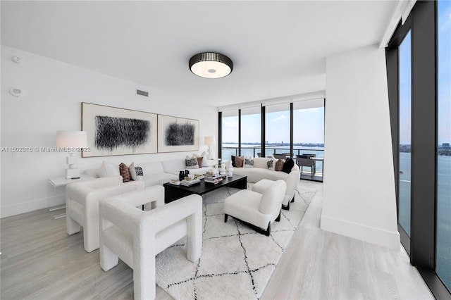 living room featuring floor to ceiling windows, light wood-type flooring, and a water view