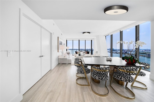 dining room featuring light wood-type flooring, expansive windows, and a water view