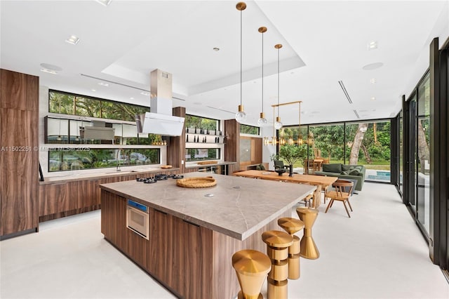 kitchen featuring a kitchen island, expansive windows, island exhaust hood, built in microwave, and a raised ceiling