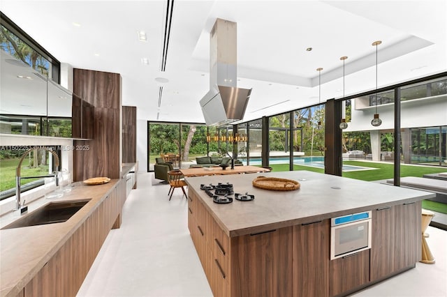 kitchen with floor to ceiling windows, sink, hanging light fixtures, a tray ceiling, and a kitchen island