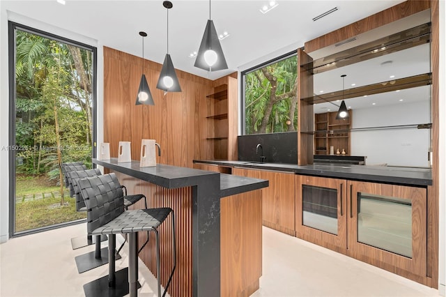 bar with floor to ceiling windows, sink, pendant lighting, and wood walls