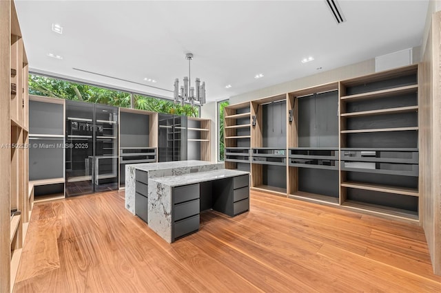 kitchen with hanging light fixtures, a center island, light stone counters, a notable chandelier, and light hardwood / wood-style floors