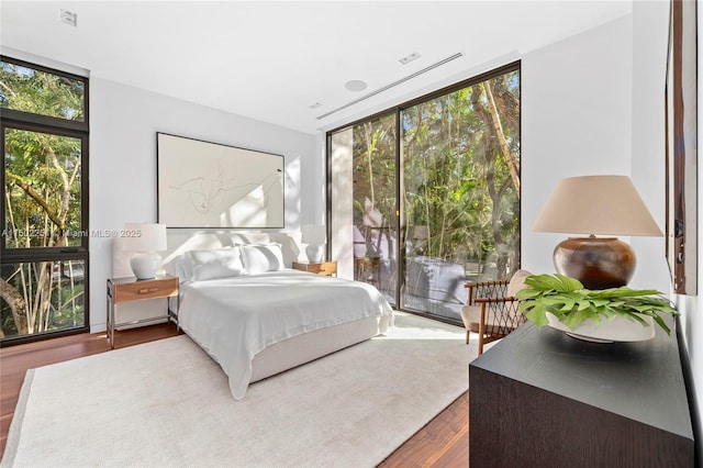 bedroom featuring expansive windows, hardwood / wood-style flooring, and access to outside