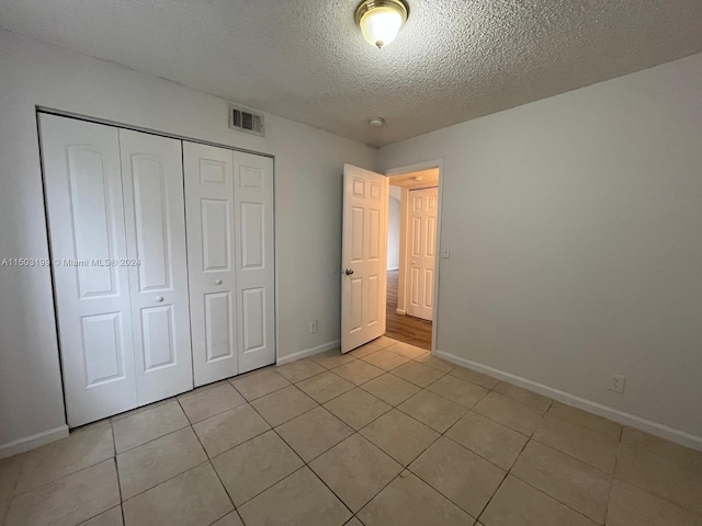 unfurnished bedroom featuring light tile patterned flooring, a textured ceiling, and a closet