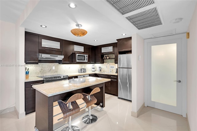 kitchen featuring a breakfast bar area, stainless steel appliances, backsplash, dark brown cabinetry, and a center island