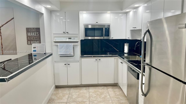 kitchen with light tile patterned flooring, sink, white cabinetry, appliances with stainless steel finishes, and backsplash