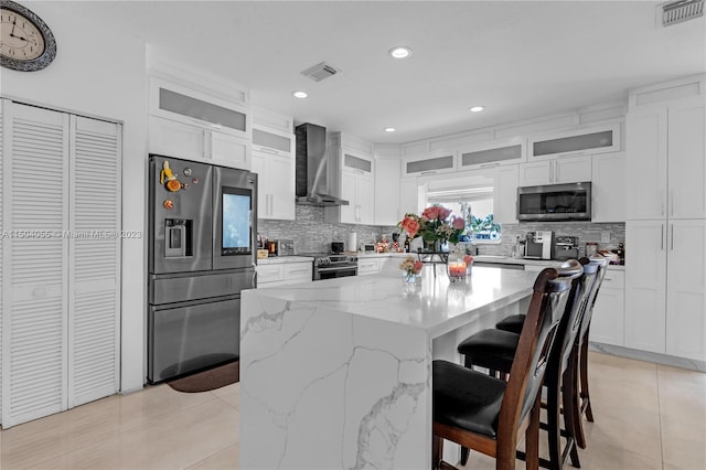 kitchen with wall chimney range hood, a kitchen island, appliances with stainless steel finishes, backsplash, and a breakfast bar