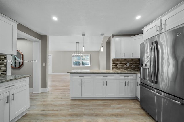 kitchen with light hardwood / wood-style flooring, tasteful backsplash, kitchen peninsula, light stone counters, and stainless steel refrigerator with ice dispenser