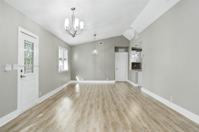 foyer entrance with vaulted ceiling, light wood-type flooring, and a chandelier