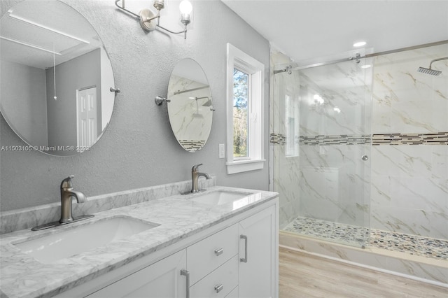 bathroom with tiled shower, wood-type flooring, and dual bowl vanity