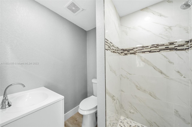 bathroom with tiled shower, hardwood / wood-style flooring, toilet, and vanity