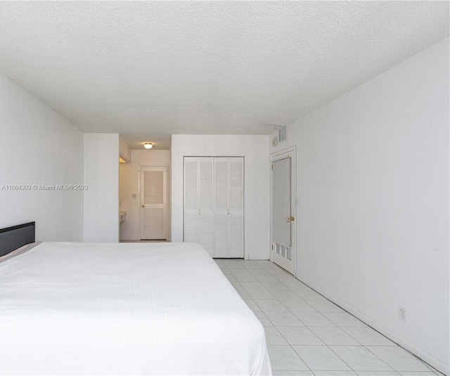 bedroom with a closet, light tile patterned floors, and a textured ceiling