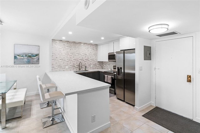 kitchen with light tile patterned flooring, white cabinets, a breakfast bar, appliances with stainless steel finishes, and backsplash