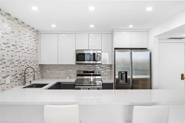 kitchen featuring white cabinetry, sink, light stone counters, appliances with stainless steel finishes, and backsplash