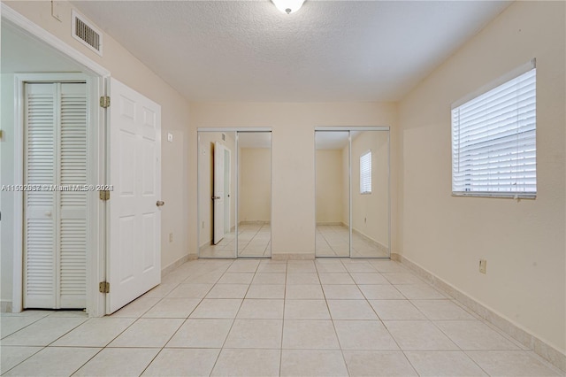 unfurnished bedroom featuring light tile floors, a textured ceiling, and two closets