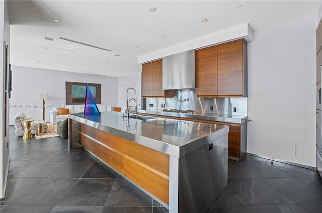 kitchen with wall chimney exhaust hood, stainless steel counters, sink, and a center island with sink