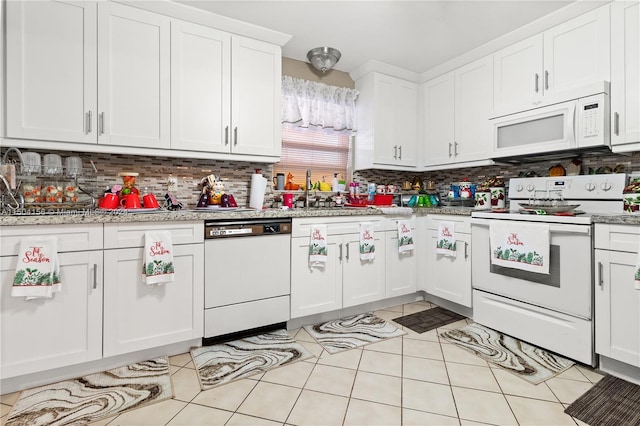 kitchen featuring white appliances, light tile patterned floors, white cabinets, decorative backsplash, and a sink