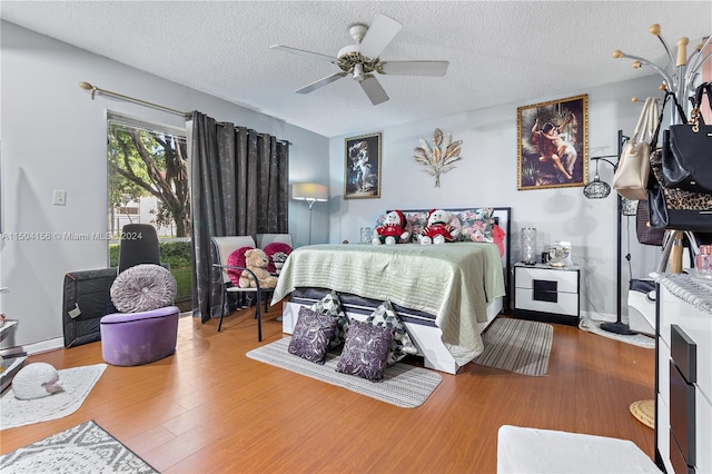 bedroom with ceiling fan, a textured ceiling, baseboards, and wood finished floors