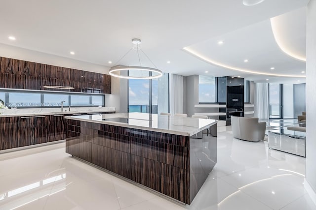 kitchen featuring light stone counters, a spacious island, light tile floors, hanging light fixtures, and sink