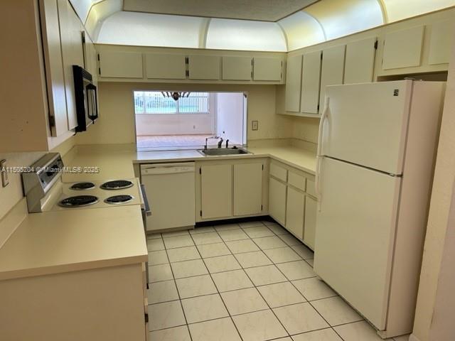 kitchen with sink, light tile patterned flooring, white appliances, and cream cabinetry