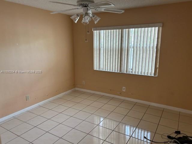 empty room featuring ceiling fan, light tile patterned flooring, and a textured ceiling