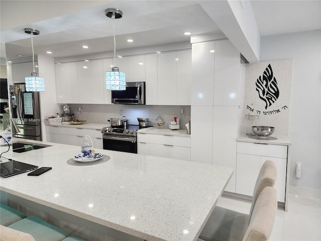 kitchen featuring a kitchen bar, white cabinets, decorative light fixtures, and appliances with stainless steel finishes