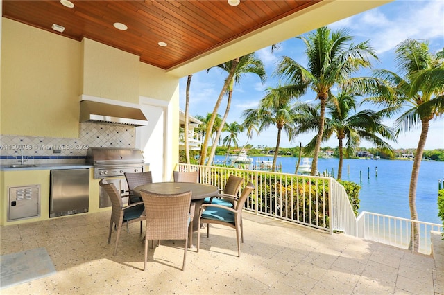 view of patio with sink, a balcony, exterior kitchen, a grill, and a water view