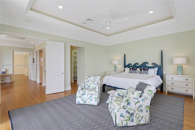 bedroom with a raised ceiling, ceiling fan, light wood-type flooring, and crown molding