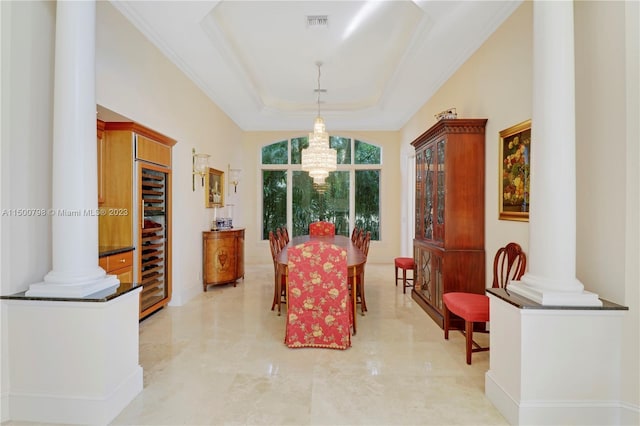 tiled dining space with beverage cooler, a raised ceiling, decorative columns, and an inviting chandelier