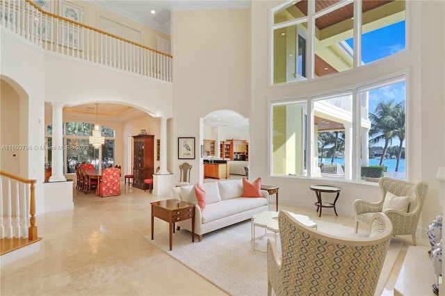 tiled living room featuring a wealth of natural light, a towering ceiling, a water view, decorative columns, and an inviting chandelier