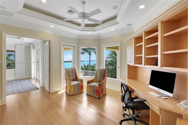 unfurnished office featuring ceiling fan, crown molding, a raised ceiling, and light wood-type flooring