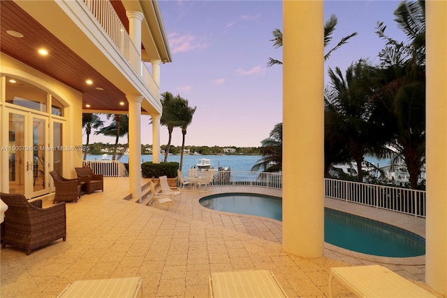 pool at dusk featuring a water view and a patio