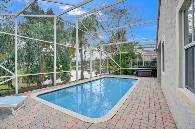 view of pool featuring glass enclosure, a water view, and a patio